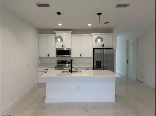 Kitchen with stainless steel appliances, white cabinetry, light marble finish floors, and an island with sink
