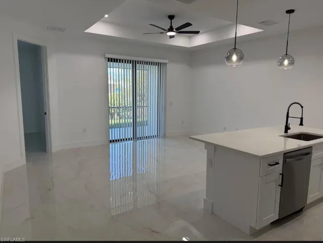 Kitchen featuring a raised ceiling, light marble finish floors, dishwasher, a ceiling fan, and light stone counters