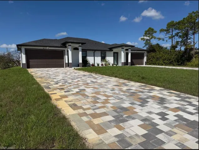 Prairie-style home featuring a front lawn, a garage, stucco siding, and driveway