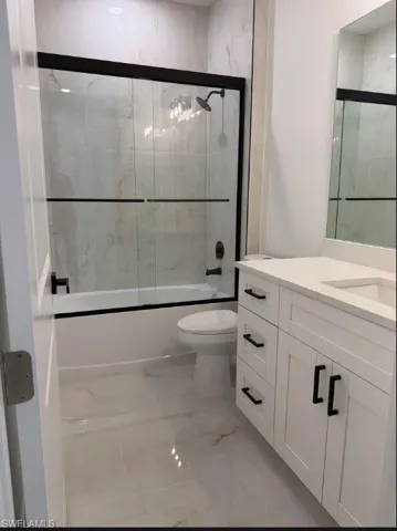 Bathroom with vanity, enclosed tub / shower combo, and light marble finish flooring