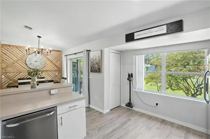 Kitchen featuring stainless steel dishwasher, a chandelier, white cabinets, light countertops, and plenty of natural light