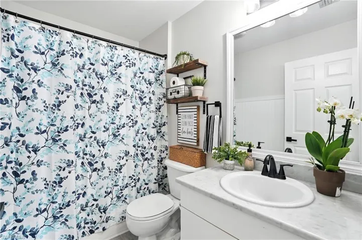 Full bath with vanity, a shower with shower curtain, and a wainscoted wall