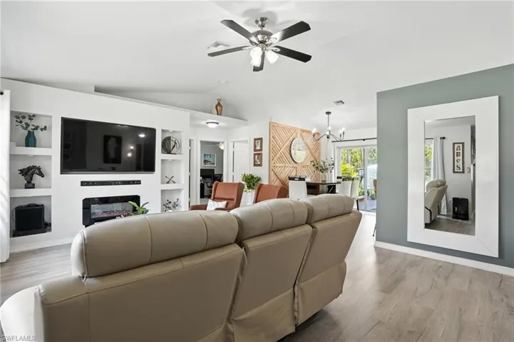 Living area featuring vaulted ceiling, a ceiling fan, wood finished floors, built in features, and a chandelier