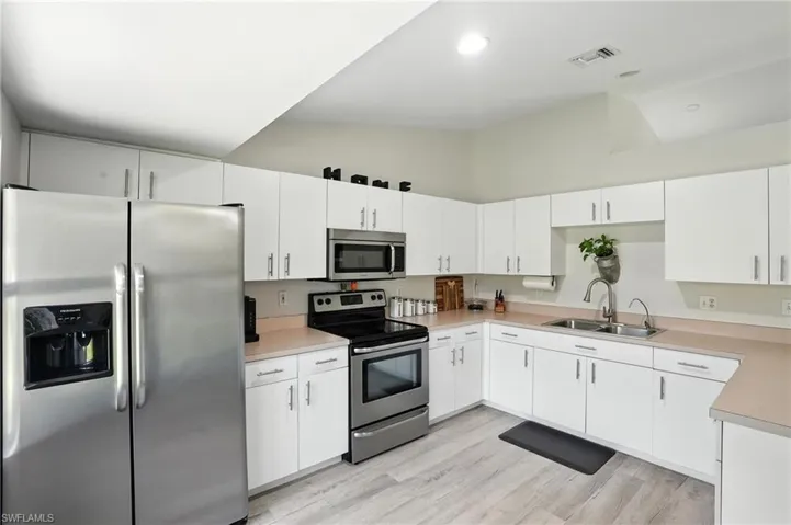 Kitchen featuring stainless steel appliances, white cabinetry, light countertops, light wood-style flooring, and high vaulted ceiling