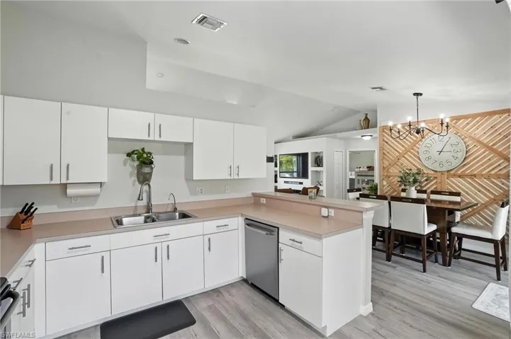 Kitchen with dishwasher, vaulted ceiling, a peninsula, light wood finished floors, and a chandelier