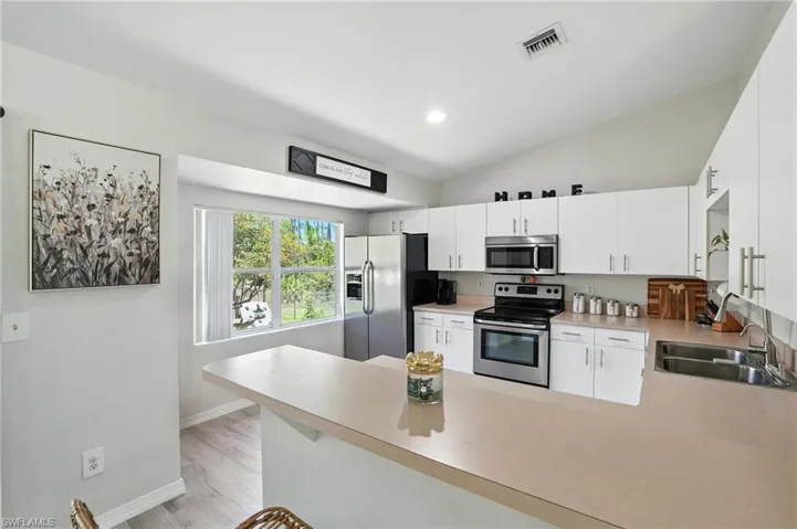 Kitchen featuring appliances with stainless steel finishes, a peninsula, light countertops, white cabinetry, and vaulted ceiling