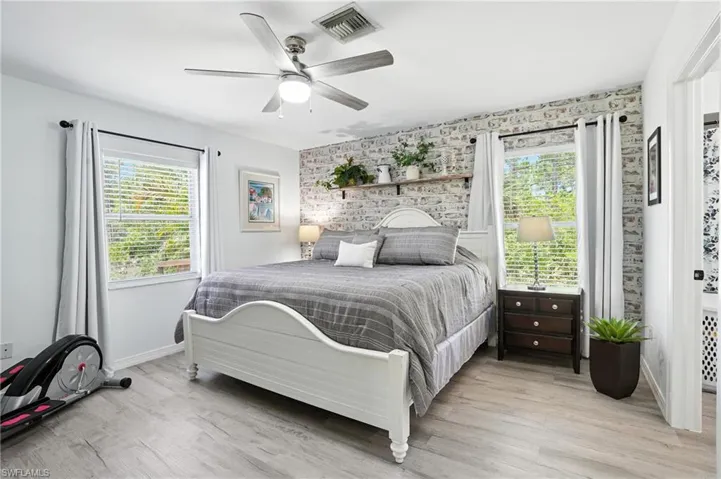 Bedroom with multiple windows, light wood-type flooring, an accent wall, and ceiling fan