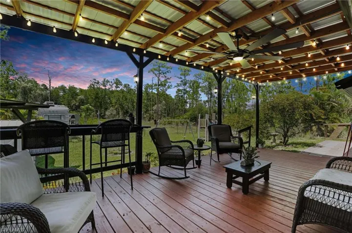 Deck at dusk with a ceiling fan, view of wooded area, an outdoor hangout area, and a yard