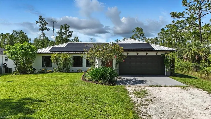 View of front of house featuring driveway, a garage, a front yard, a metal roof, and roof mounted solar panels