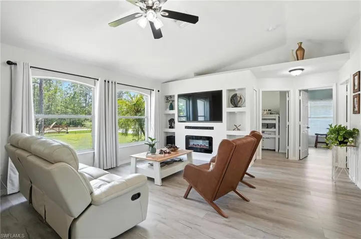 Living room with a glass covered fireplace, lofted ceiling, ceiling fan, healthy amount of natural light, and light wood-style flooring