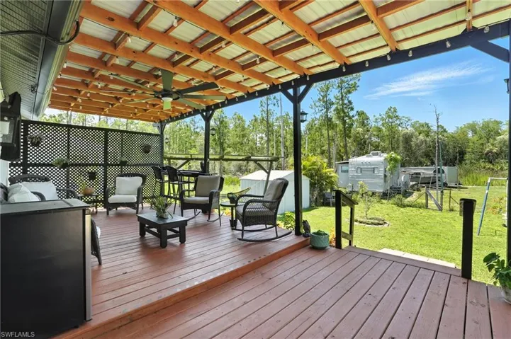 Wooden deck with an outdoor living space, a lawn, a ceiling fan, and view of wooded area