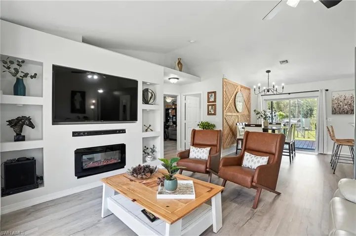 Living area featuring light wood-type flooring, a chandelier, a glass covered fireplace, vaulted ceiling, and built in shelves