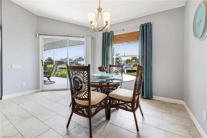 Light-toned rectangular tile flooring, sliding glass door leading to an outdoor patio, window with bamboo blinds, and a built-in ceiling light fixture