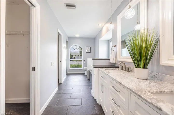 Vanity with a light-toned countertop and an undermount sink, complemented by a large mirror and pendant lighting