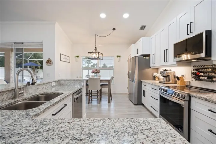 Kitchen with appliances with stainless steel finishes, ornamental molding, pendant lighting, light stone counters, and recessed lighting