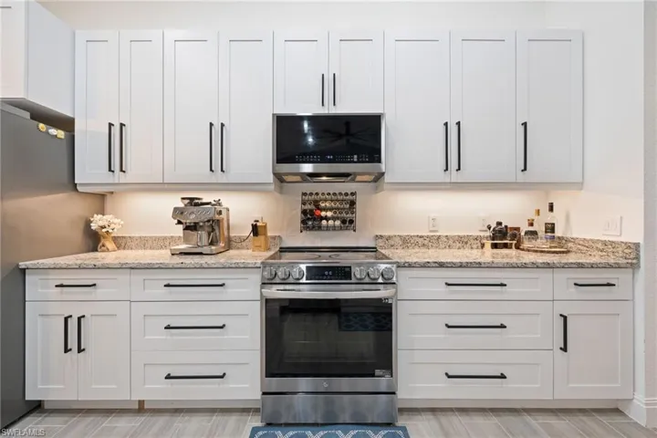 Kitchen with stainless steel appliances, light stone countertops, and white cabinets