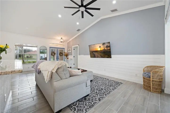 Living area featuring crown molding, a wainscoted wall, vaulted ceiling, wood tiled floors, and ceiling fan