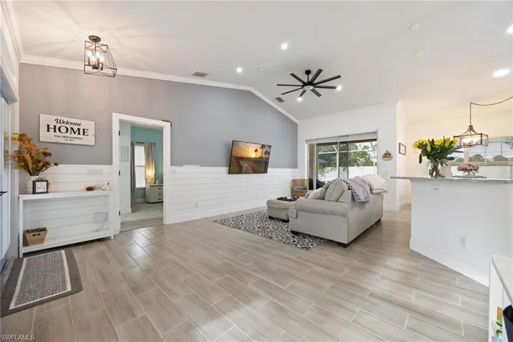 Living area with a chandelier, ornamental molding, wood finish floors, lofted ceiling, and recessed lighting