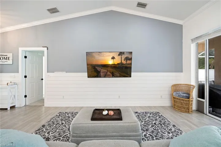 Living room featuring crown molding, wood finish floors, a wainscoted wall, and lofted ceiling