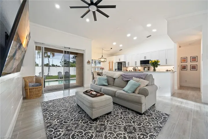 Living room with wood finish floors, recessed lighting, lofted ceiling, a ceiling fan, and ornamental molding