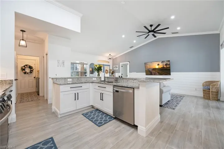 Kitchen featuring light stone counters, ornamental molding, stainless steel appliances, wood finish floors, and white cabinetry