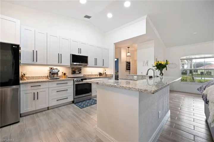 Kitchen with ornamental molding, appliances with stainless steel finishes, light stone countertops, wood tiled floors, and a kitchen island with sink