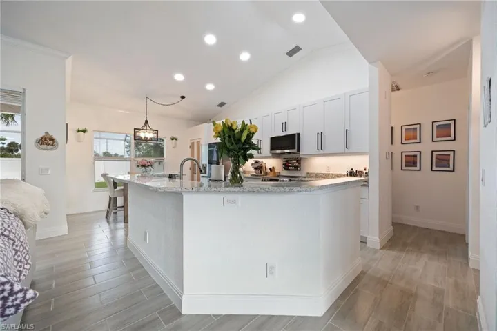 Kitchen featuring wood tiled floors, recessed lighting, hanging light fixtures, light stone counters, and a kitchen island with sink
