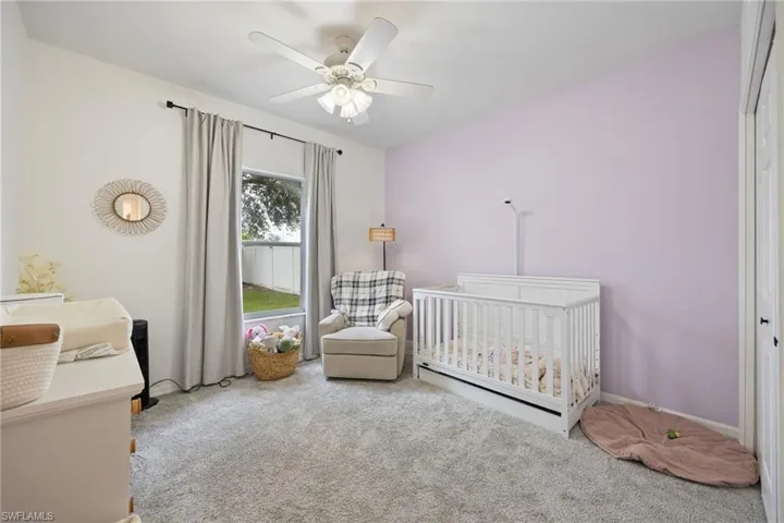 Carpeted bedroom featuring a nursery area and ceiling fan