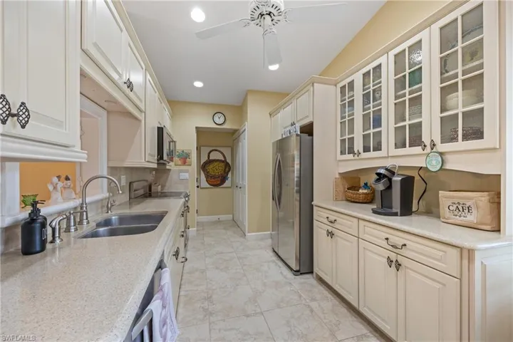 Kitchen with appliances with stainless steel finishes, sink, light stone counters, light tile patterned flooring, and ceiling fan