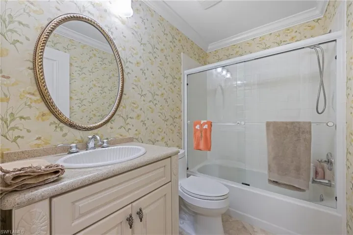 Full bathroom with enclosed tub / shower combo, crown molding, tile patterned floors, toilet, and vanity