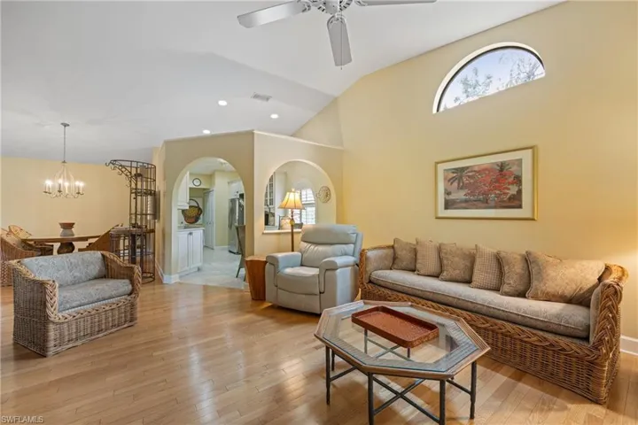 Living room with wood-type flooring, ceiling fan with notable chandelier, and vaulted ceiling