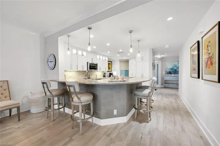 Kitchen featuring a breakfast bar, white cabinetry, hanging light fixtures, kitchen peninsula, and light stone countertops