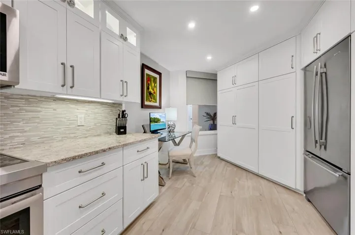 Kitchen featuring light stone counters, stainless steel fridge, white cabinets, and light wood-type flooring
