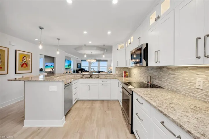 Kitchen with appliances with stainless steel finishes, light stone counters, white cabinets, decorative light fixtures, and light wood-type flooring