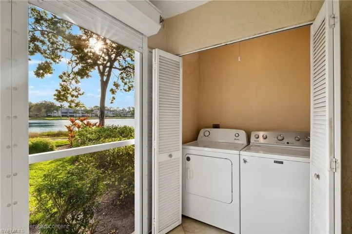 Washroom featuring washing machine and dryer, a water view, a healthy amount of sunlight, and light tile patterned floors