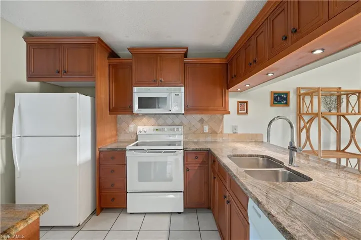 Kitchen featuring light tile patterned flooring, a textured ceiling, white appliances, and sink
