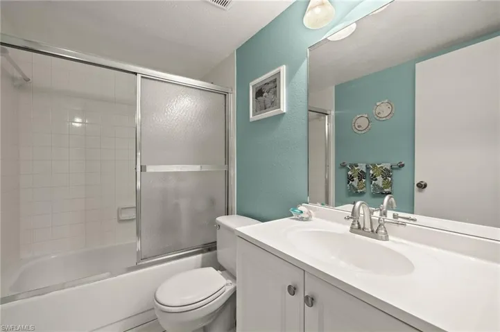 Full bathroom with vanity, bath / shower combo with glass door, a textured ceiling, and toilet