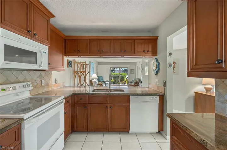 Kitchen featuring a textured ceiling, white appliances, sink, and light tile patterned floors