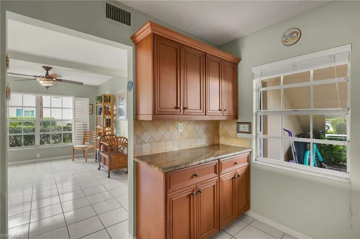 Kitchen featuring decorative backsplash, ceiling fan, dark stone countertops, light tile patterned floors, and a textured ceiling