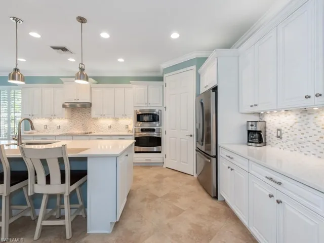 Kitchen with decorative light fixtures, stainless steel appliances, a center island with sink, and backsplash
