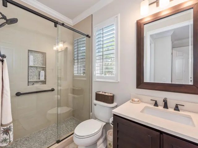 Bathroom with crown molding, a shower with door, vanity, and toilet