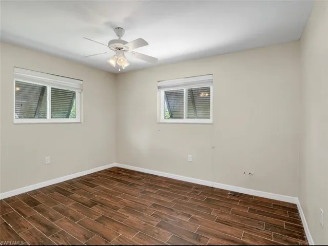 Unfurnished room with baseboards, dark wood-type flooring, and a ceiling fan