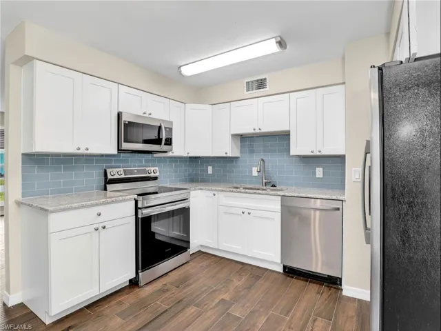 Kitchen featuring dark wood-style flooring, stainless steel appliances, backsplash, a sink, and visible vents