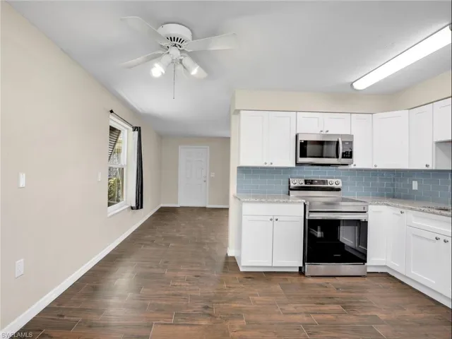 Kitchen featuring backsplash, white cabinets, stainless steel appliances, and dark wood-style floors