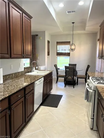 Kitchen with sink, white dishwasher, a tray ceiling, gas range, and light tile patterned flooring