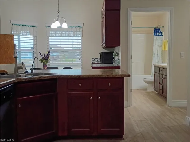 Kitchen featuring reddish brown cabinets, pendant lighting, black dishwasher, and light wood-style flooring