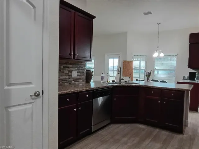 Kitchen featuring tasteful backsplash, a chandelier, dishwasher, a peninsula, and pendant lighting