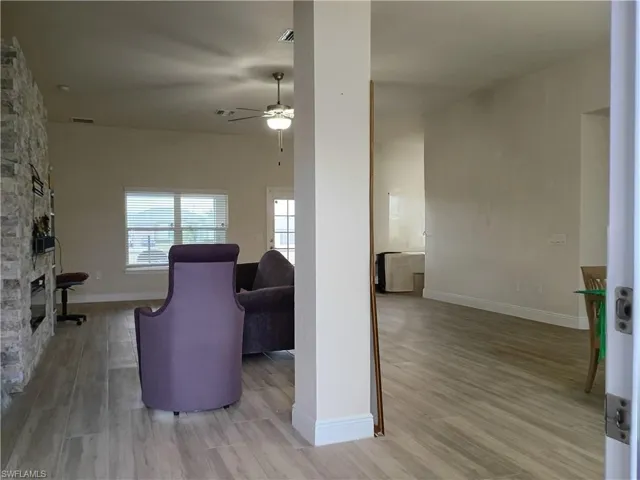 Living area featuring light wood-type flooring, ceiling fan, and a stone fireplace