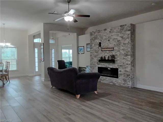 Living area featuring ceiling fan, wood finished floors, a stone fireplace, and a chandelier
