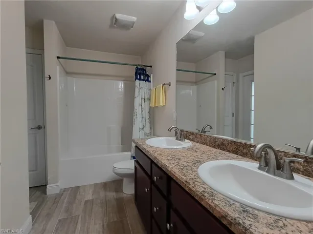 Bathroom with double vanity, shower / tub combo with curtain, and light wood-type flooring